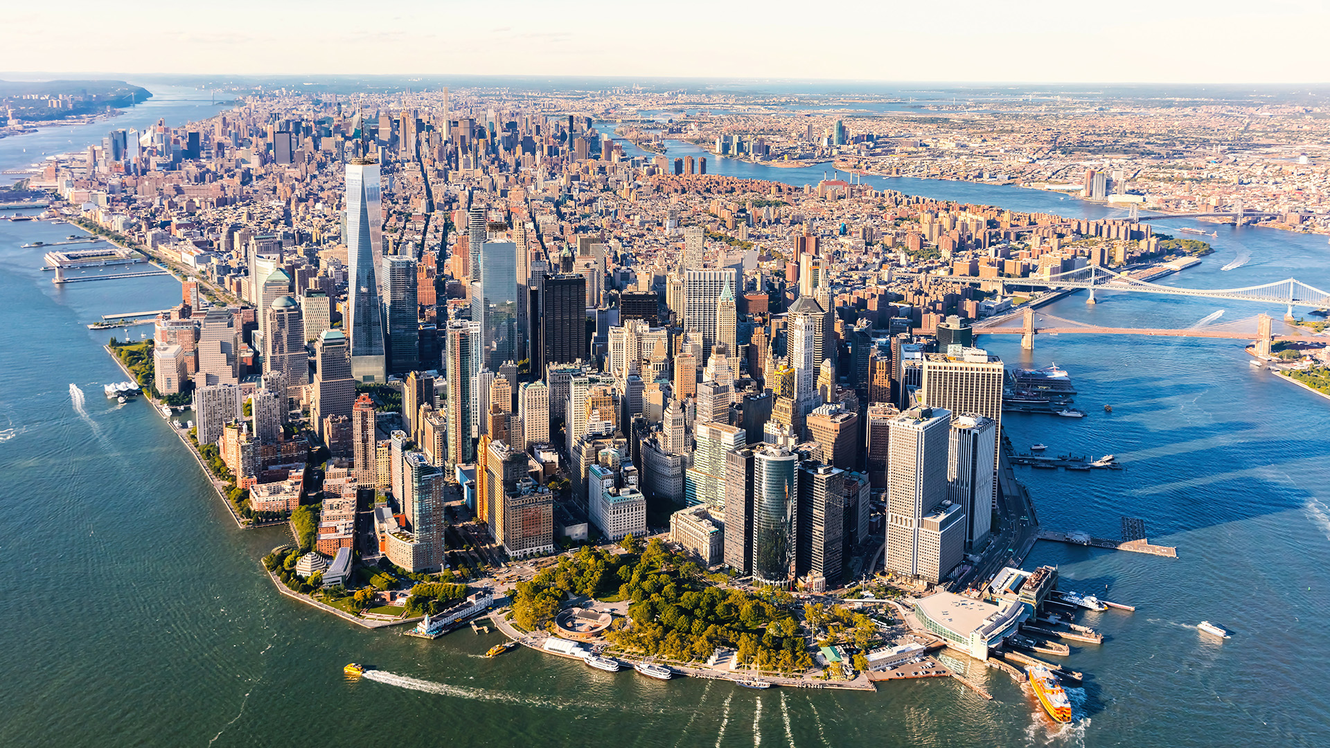 The image shows an aerial view of a city skyline with numerous high-rise buildings, including recognizable landmarks such as the Empire State Building and the Statue of Liberty in the distance, with water bodies interspersed among the urban landscape.