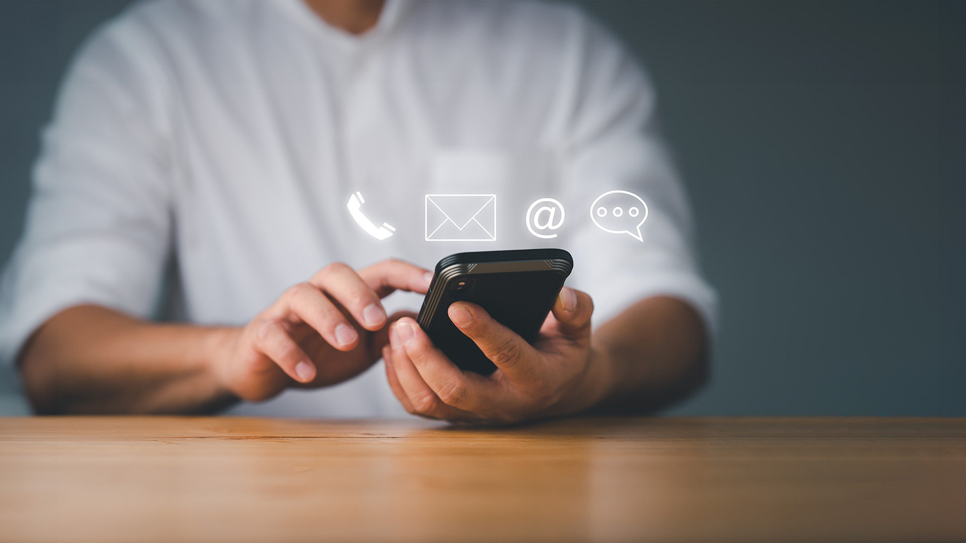 The image shows a person using a smartphone while seated at a table.