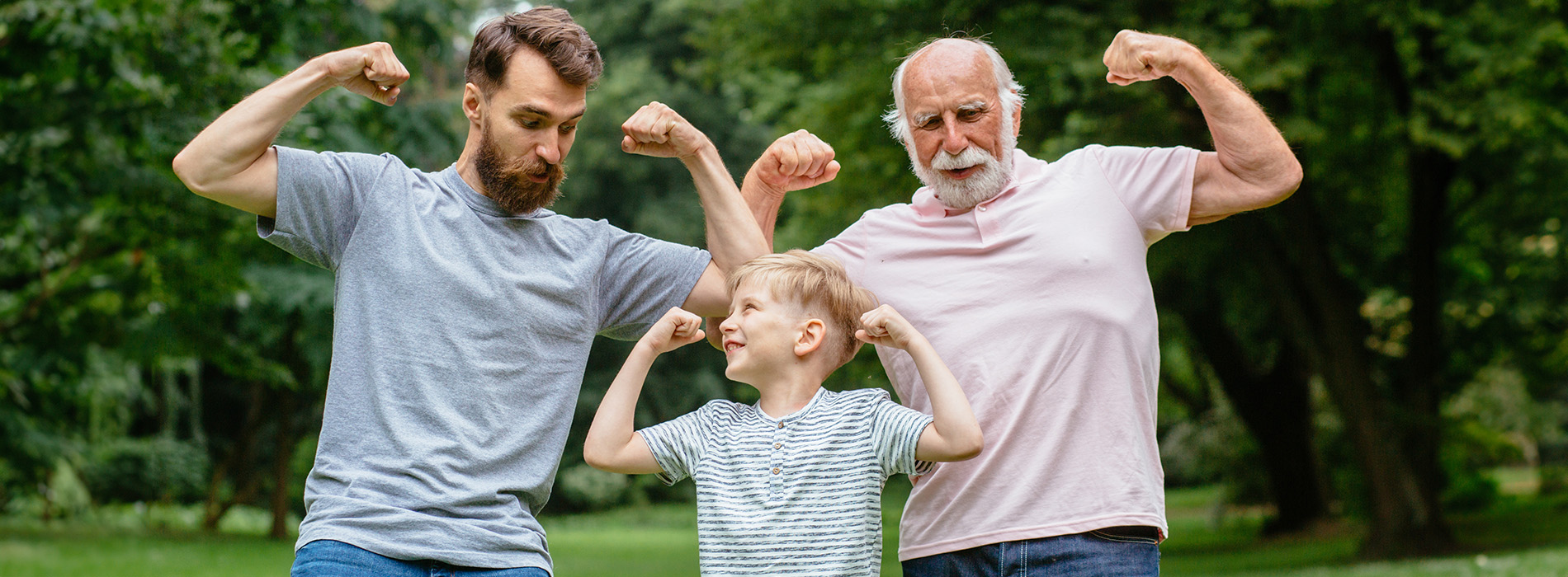 The image shows three people posing together outdoors  two adults are flexing their muscles while standing with a child, who appears to be watching them.