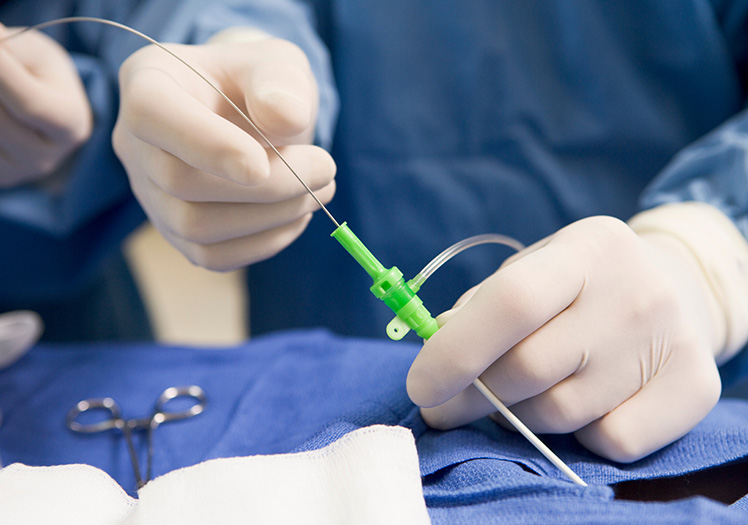 The image depicts a medical setting with a person wearing gloves and surgical attire performing a procedure on a patient, involving the use of medical instruments such as scissors and an IV drip.