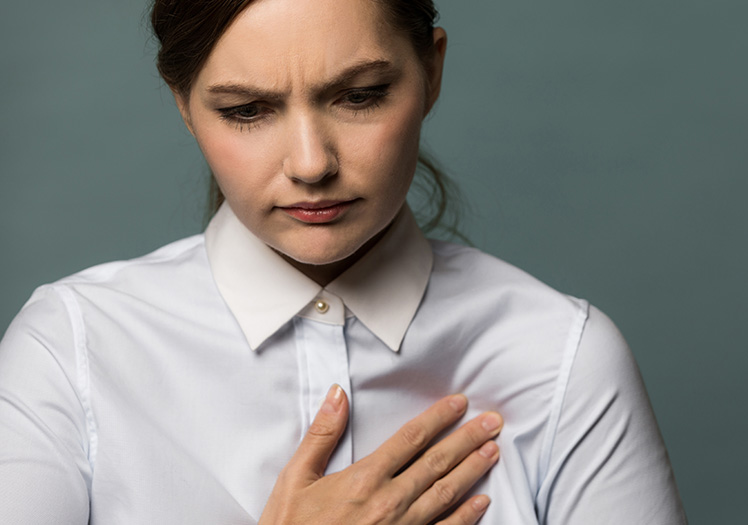 A woman with her hand on her chest, looking concerned or pained.